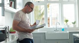 Man reading documents while standing in his kitchen.