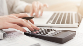 Close-up of a woman’s hands using a laptop and a calculator.