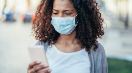 Une femme regardant son téléphone tout en portant un masque.