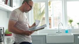 Un homme lisant des documents debout dans sa cuisine.