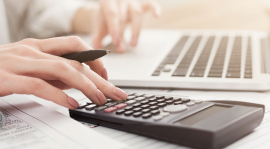 Gros plan des mains d'une femme utilisant un ordinateur portable et une calculatrice.