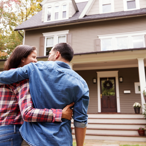 Couple looking at the front of their new home with their arms around each other.