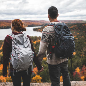 A hiking couple on a rocky hilltop admiring the autumn colours in the forest below.
