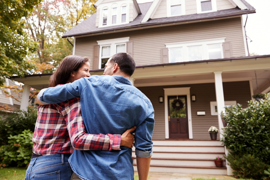 Un couple regardant la façade de leur maison en se tenant le bras.