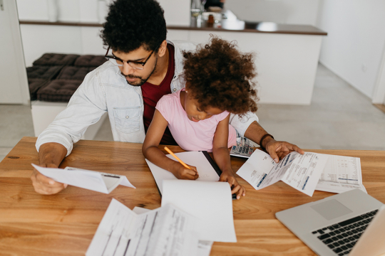 Father reading financial documents while his young daughter draws a picture.