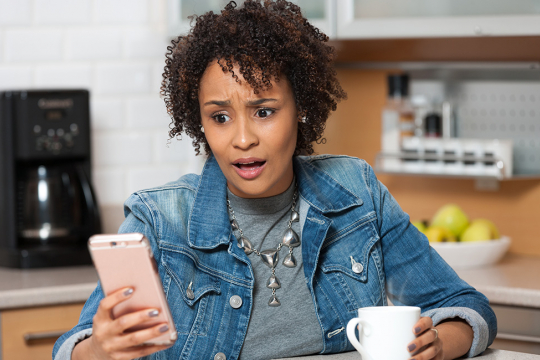 Woman looking at her phone with a shocked expression.