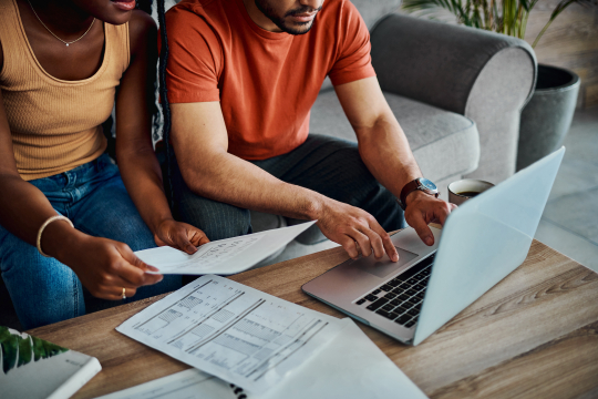 Couple sitting on a couch using a laptop and reviewing bills. 