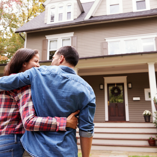 Couple looking at the front of their new home with their arms around each other.