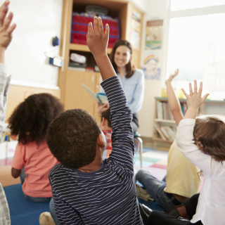 Young students with their hands raised.