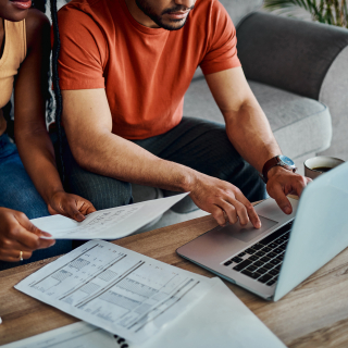 Couple sitting on a couch using a laptop and reviewing bills. 