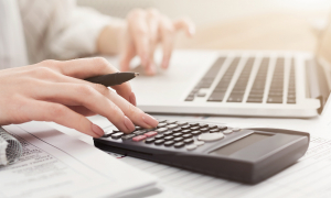 Close-up of a woman’s hands using a laptop and a calculator.