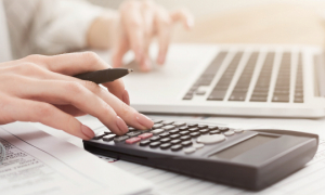 Gros plan des mains d'une femme utilisant un ordinateur portable et une calculatrice.